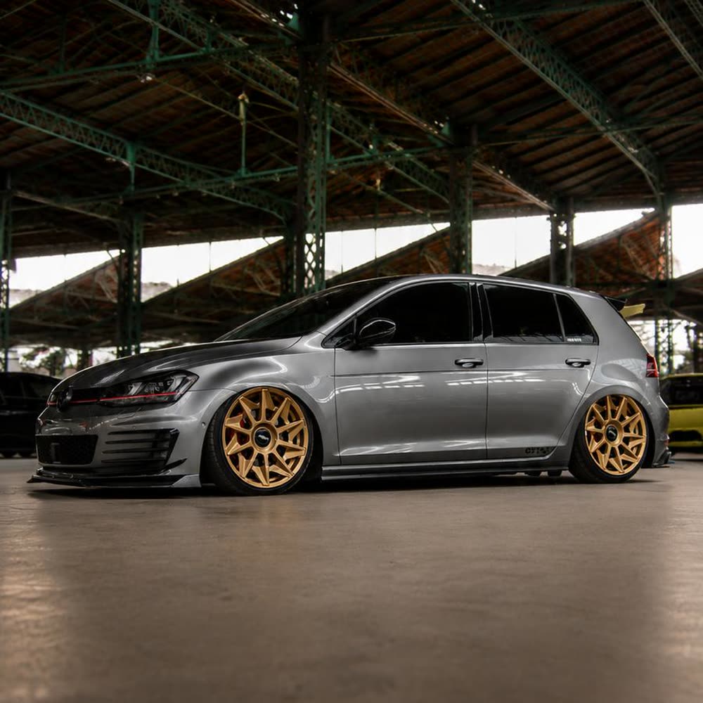 Volkswagen Golf GTI gris con llantas doradas en una nave